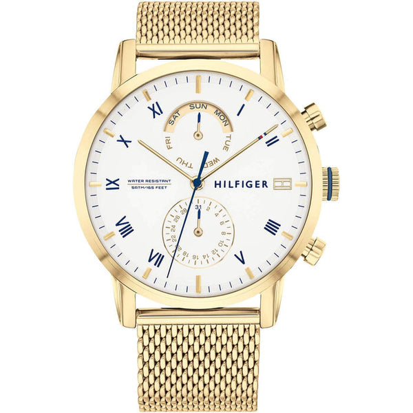A gold-plated Tommy Hilfiger men's watch with a 44mm round case and a white dial. The watch features blue Roman numerals and gold-tone hour markers, with three subdials displaying the day of the week, date, and 24-hour time. It has gold-tone hour and minute hands, a slim blue second hand, and the "Hilfiger" logo in blue on the right side. The watch includes a woven gold mesh strap and three pushers on the right side of the case. The overall design is elegant and refined.