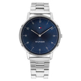A minimalist Tommy Hilfiger men's watch with a 41mm round stainless steel case and a polished silver metal bracelet. The watch features a deep blue sunray dial with small silver Arabic numerals, slim hour markers, and sleek silver hands. The Tommy Hilfiger flag logo is positioned at the 12 o'clock mark, and the word "HILFIGER" is printed above the 6 o'clock position. The design is clean, elegant, and modern.
