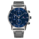 A Tommy Hilfiger men's watch with a 44mm round stainless steel case and a polished gunmetal bracelet. The watch features a deep blue dial with silver-tone Roman numeral hour markers and three subdials showing day of the week, date, and 24-hour time. It includes silver-tone hands and a slender second hand, with the Tommy Hilfiger flag logo and "Hilfiger" branding on the right side of the dial. The design is sleek, modern, and sophisticated.