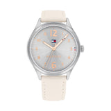 A Tommy Hilfiger women's watch with a 38mm silver-tone stainless steel case and a soft beige leather strap with matching stitching. The dial features a subtle sunburst pattern in silver with rose gold-tone Arabic numerals, hands, and markers. The Tommy Hilfiger flag logo is placed just below the 12 o’clock position, with the word “HILFIGER” above the 6 o’clock mark. The design is feminine, elegant, and minimalistic.