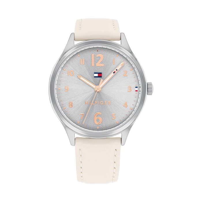 A Tommy Hilfiger women's watch with a 38mm silver-tone stainless steel case and a soft beige leather strap with matching stitching. The dial features a subtle sunburst pattern in silver with rose gold-tone Arabic numerals, hands, and markers. The Tommy Hilfiger flag logo is placed just below the 12 o’clock position, with the word “HILFIGER” above the 6 o’clock mark. The design is feminine, elegant, and minimalistic.